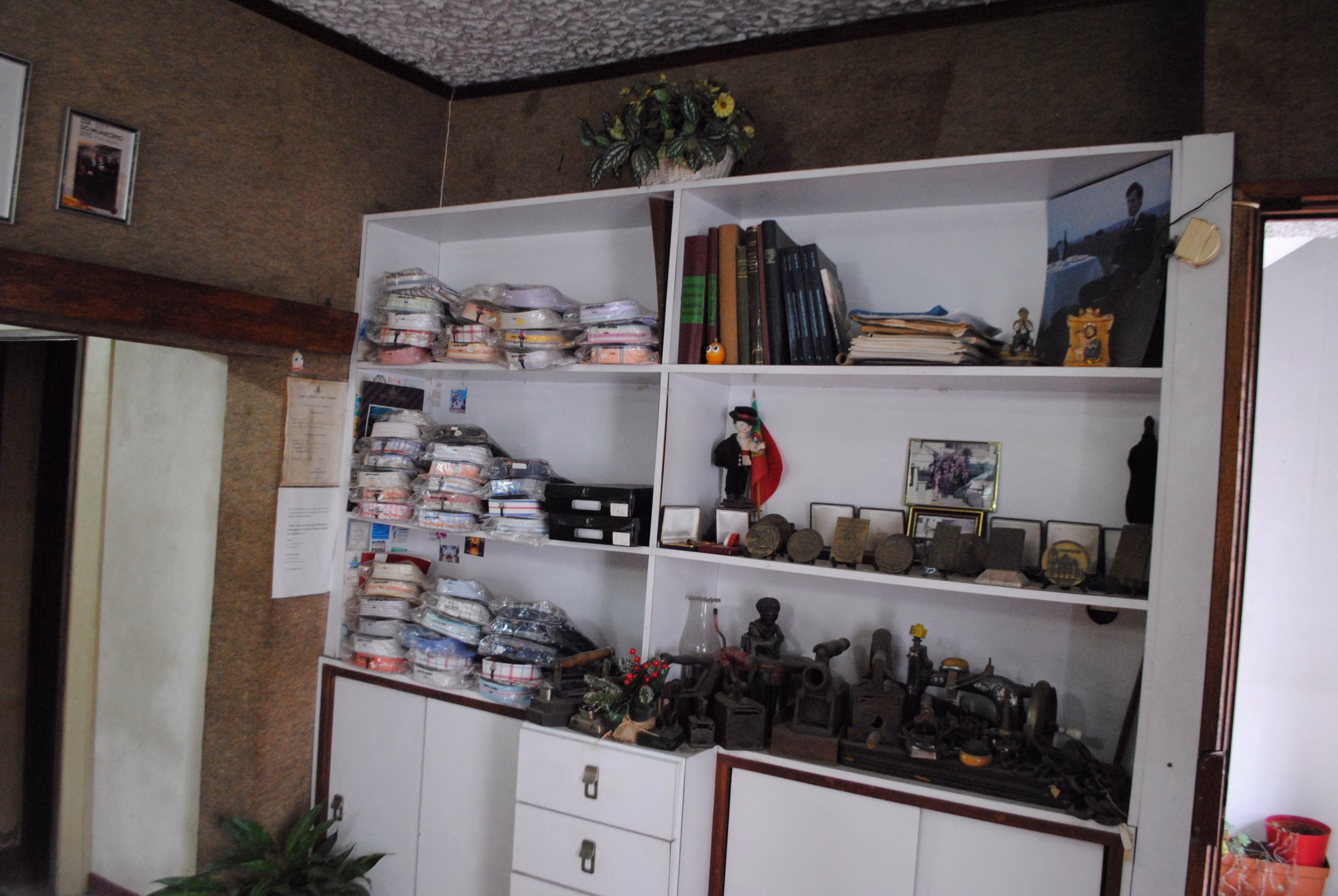 Armário no interior da Alfaiataria Moderna, com medalhas, camisas, livros e ferros de engomar.