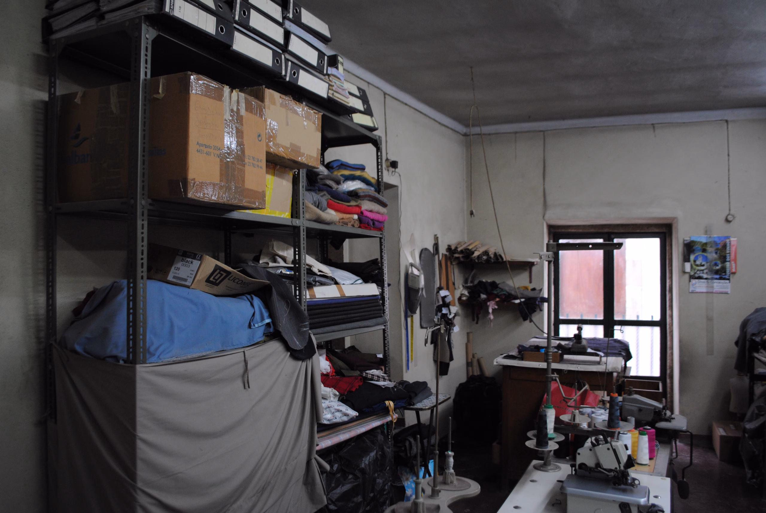 Interior da oficina da Alfaiataria Moderna, com maquinas de costura, trabalho a ser feito e casacos.